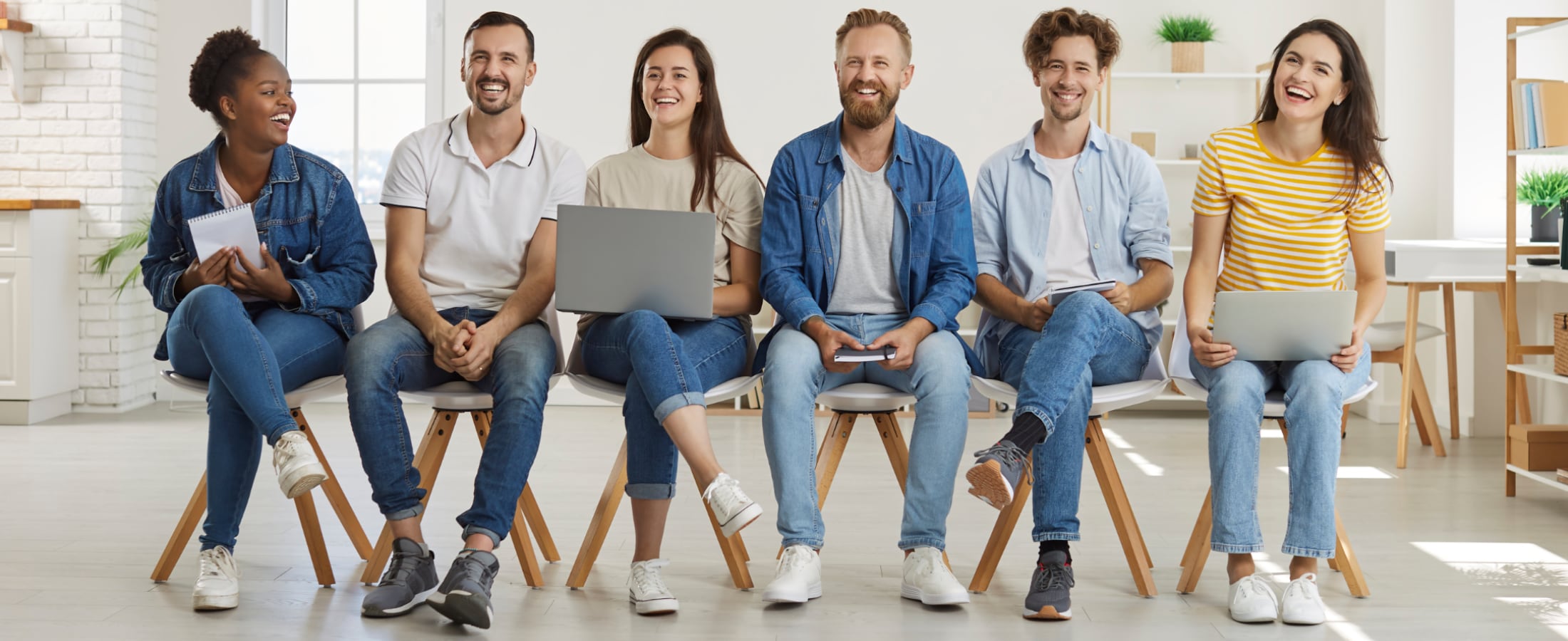 Gruppe von Bewerberinnen und Bewerbern sitzen in einer Reihe und lachen